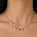 A gold-plated stainless steel chain for women featuring a curved arrangement of pearls and five dangling bezel-set crystal charms, shown on a model