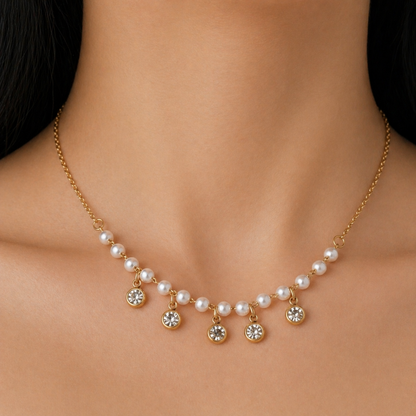 A gold-plated stainless steel chain for women featuring a curved arrangement of pearls and five dangling bezel-set crystal charms, shown on a model