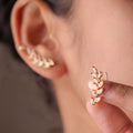 A pair of gold-plated laurel vine ear climber earrings for women featuring sparkling marquise-cut white leaves on a model
