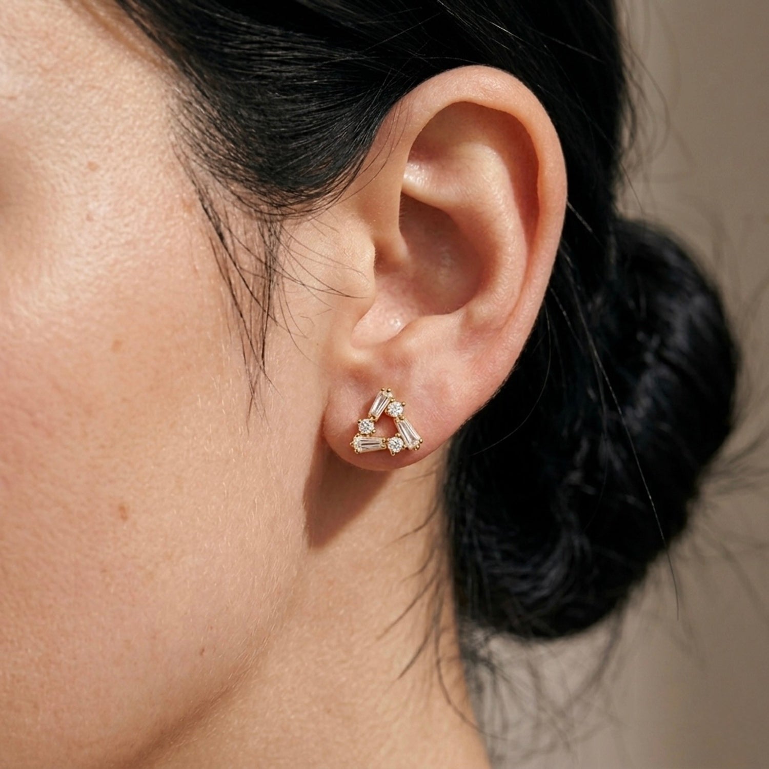 A gold-plated triangle stud earrings for women featuring a mix of baguette and round-cut crystals, shown on a model