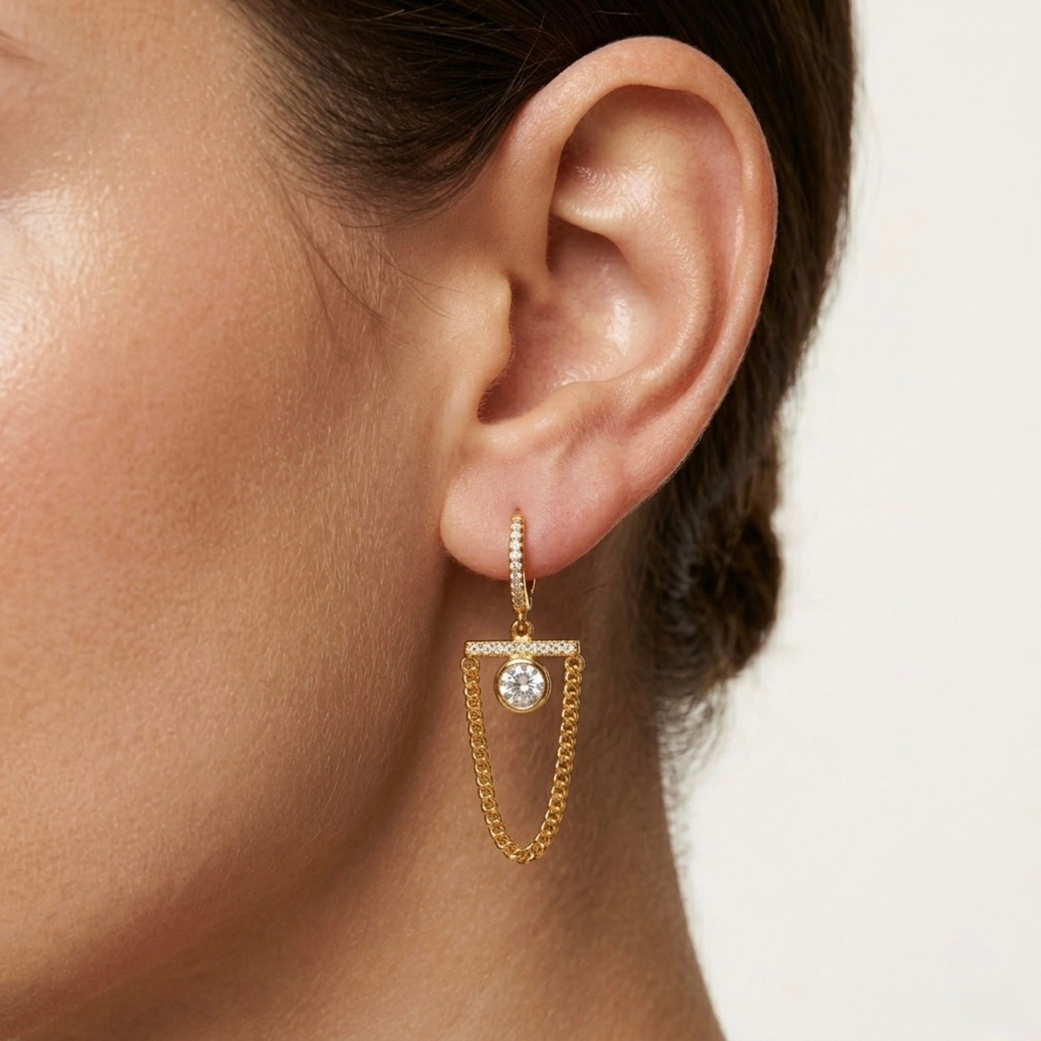 A pair of gold-plated long earrings for women featuring a hoop, a horizontal crystal bar, and a dangling gold curb chain loop, shown on a model