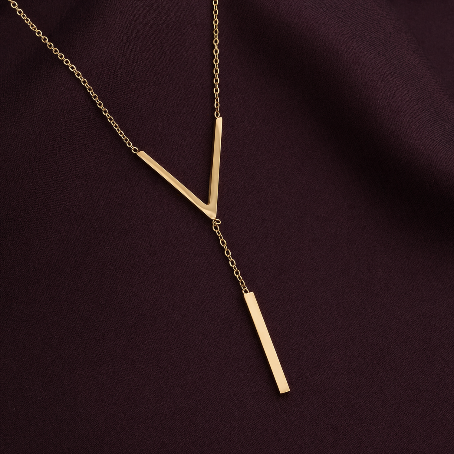 A close-view of a gold-plated stainless steel chain for women featuring a minimalist V-chevron and a long vertical bar pendant