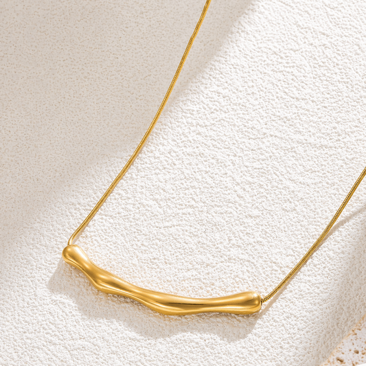 A close-view of a gold-plated stainless steel chain for women featuring a horizontal, fluid-shaped "liquid gold" ripple bar pendant on a sleek snake chain