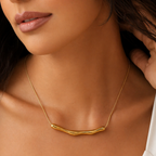 A gold-plated stainless steel chain for women featuring a horizontal, fluid-shaped "liquid gold" ripple bar pendant on a sleek snake chain shown on a model