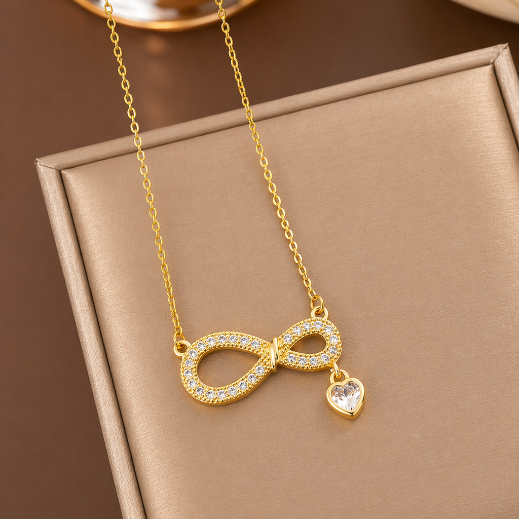 A gold-plated stainless steel chain for women featuring an infinity symbol pendant set with sparkling crystals and a small dangling heart-shaped crystal charm.