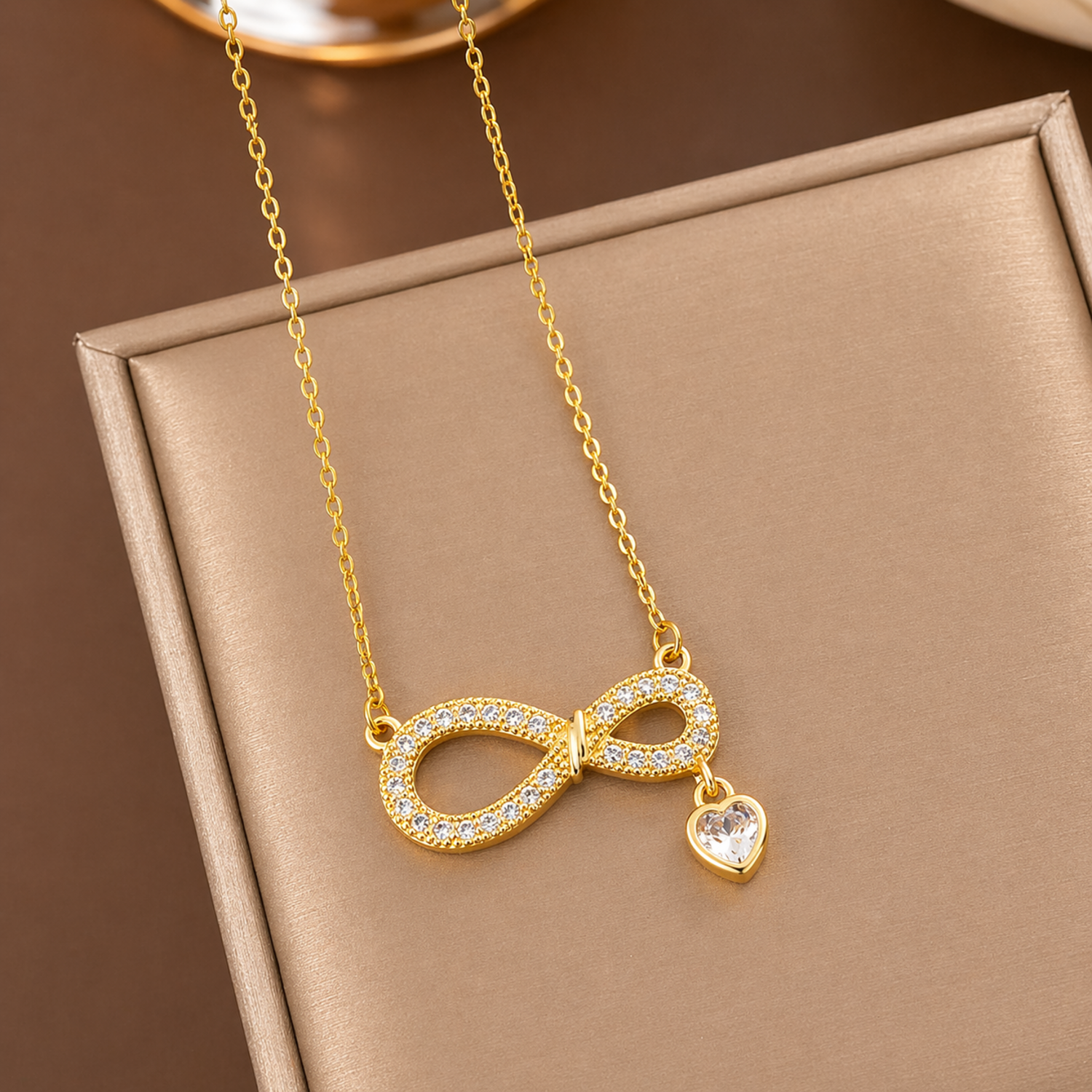A gold-plated stainless steel chain for women featuring an infinity symbol pendant set with sparkling crystals and a small dangling heart-shaped crystal charm.