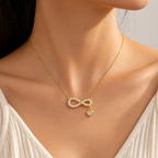 A gold-plated stainless steel chain for women featuring an infinity symbol pendant set with sparkling crystals and a small dangling heart-shaped crystal charm shown on a model