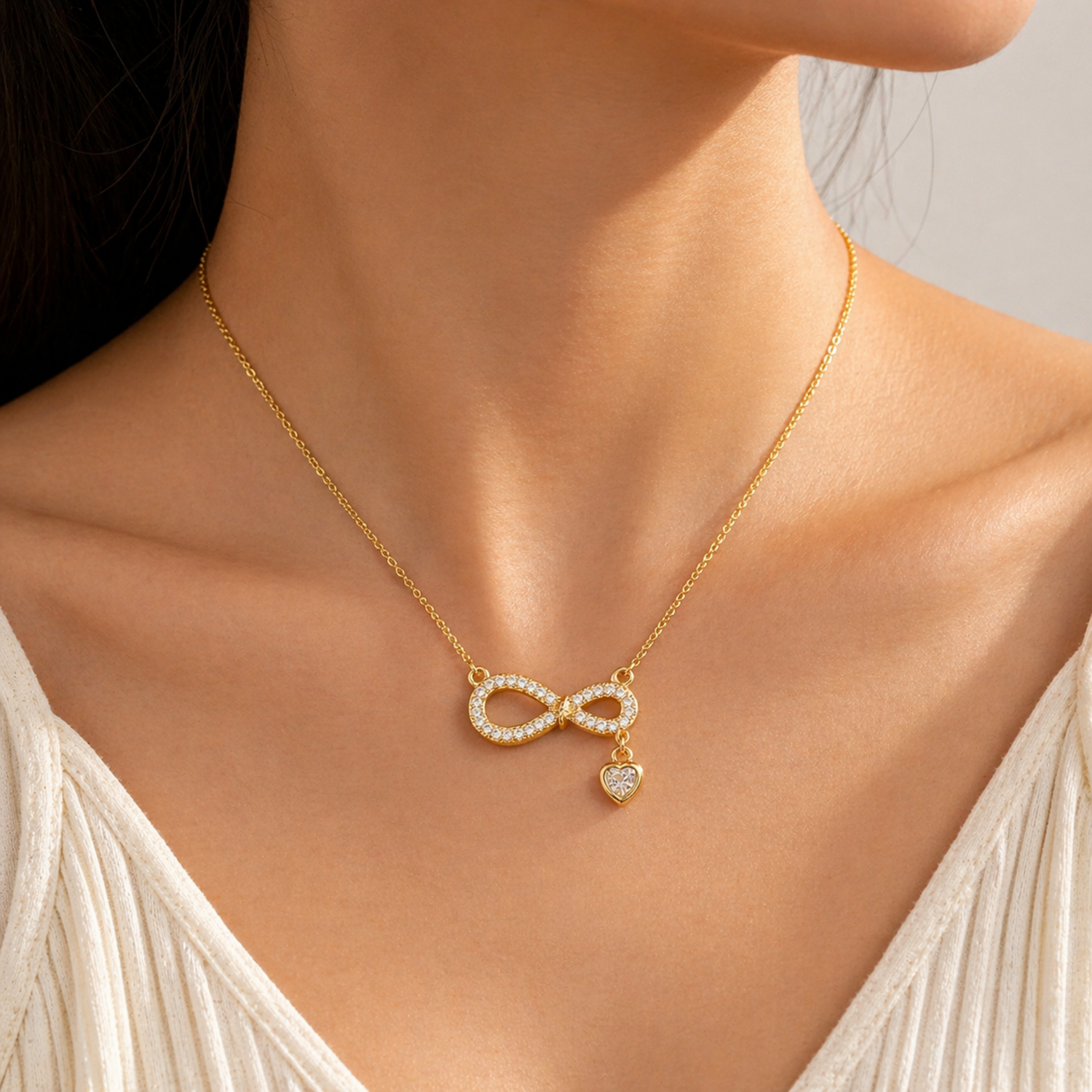 A gold-plated stainless steel chain for women featuring an infinity symbol pendant set with sparkling crystals and a small dangling heart-shaped crystal charm shown on a model
