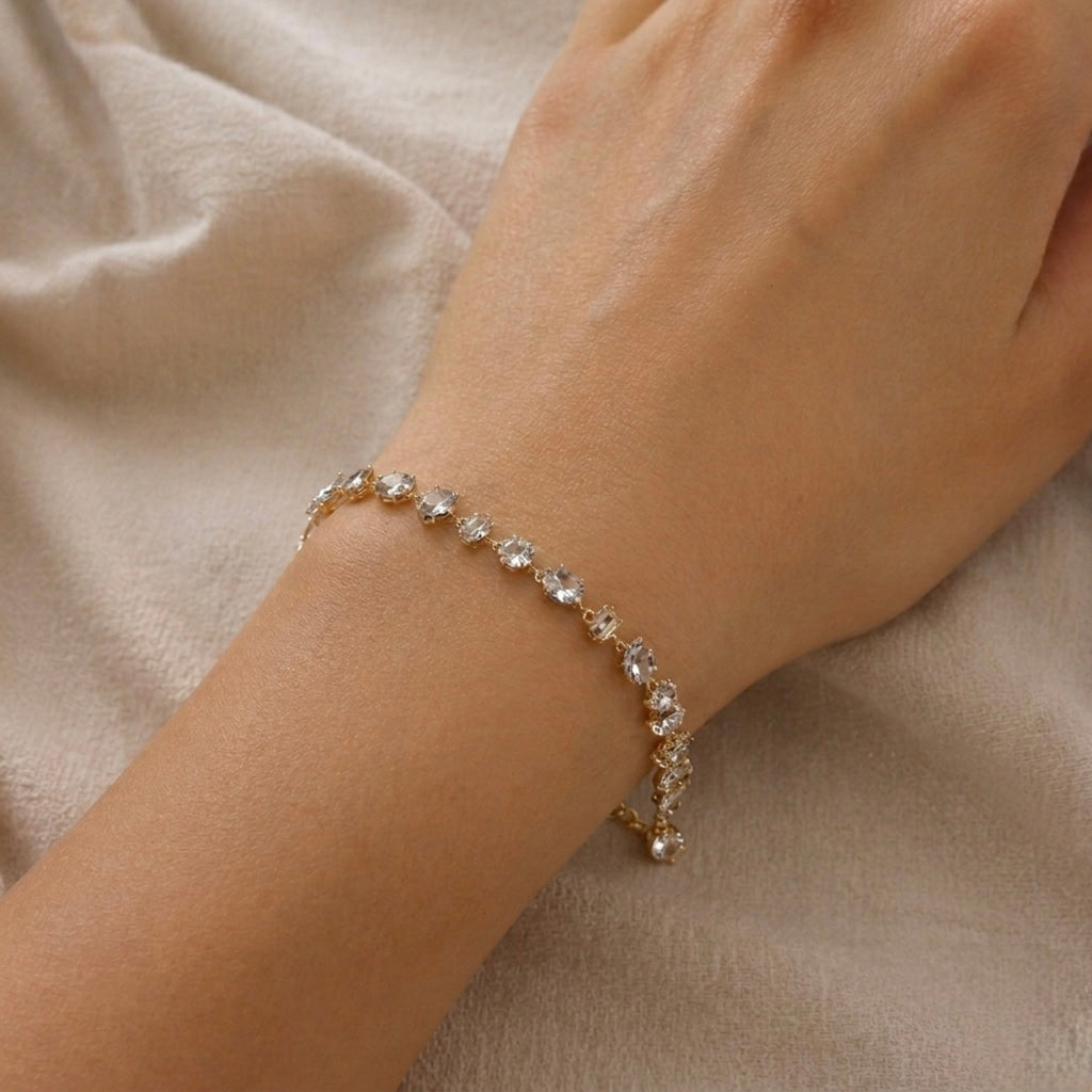 A gold-plated chain bracelet for women featuring an intricate mix of clear multi-shape stones, including brilliant, emerald, oval, and princess cuts, on a model