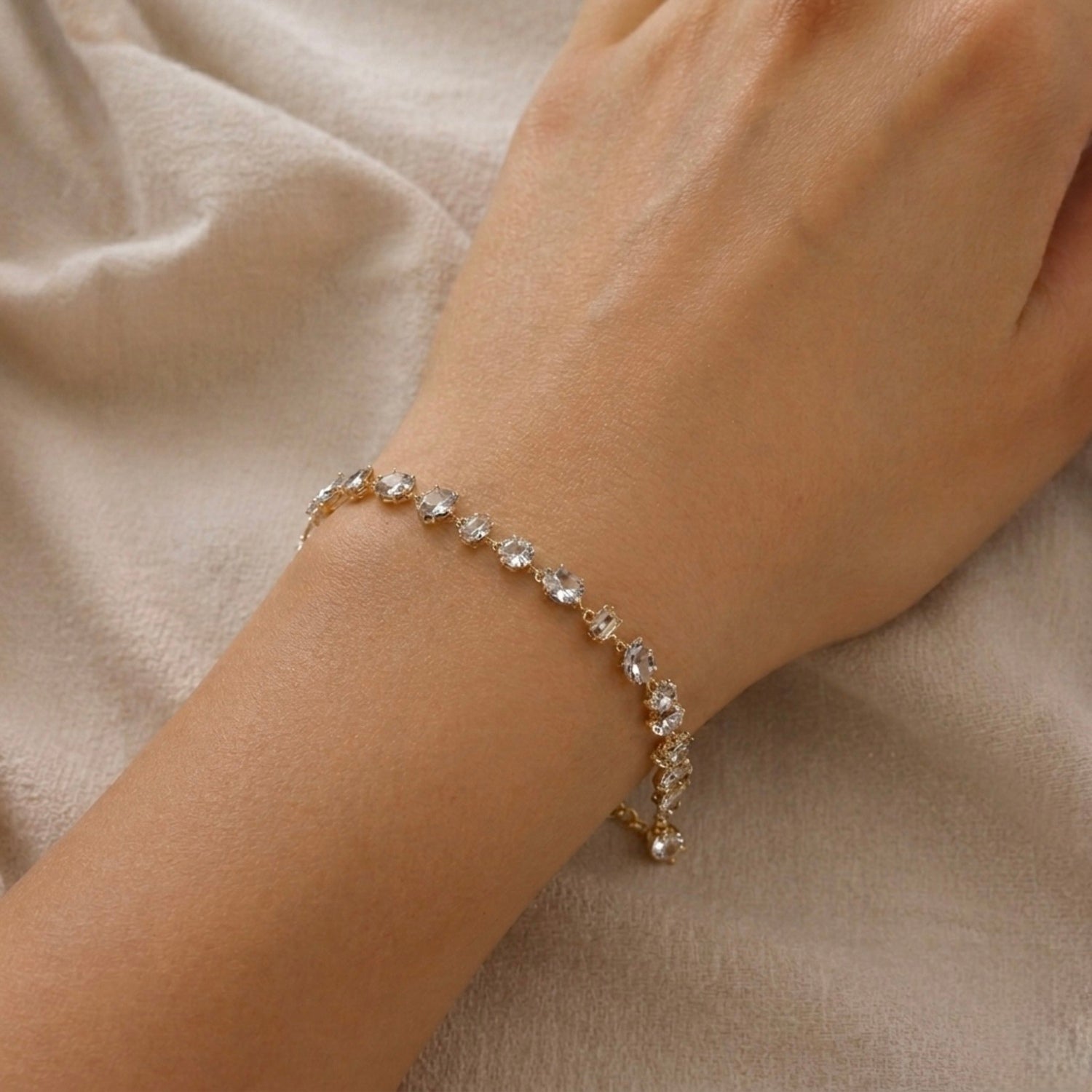 A gold-plated chain bracelet for women featuring an intricate mix of clear multi-shape stones, including brilliant, emerald, oval, and princess cuts, on a model