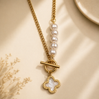 A close-view of a gold-plated stainless steel chain for women featuring an asymmetrical pearl accent, a toggle clasp, and a mother-of-pearl clover charm.