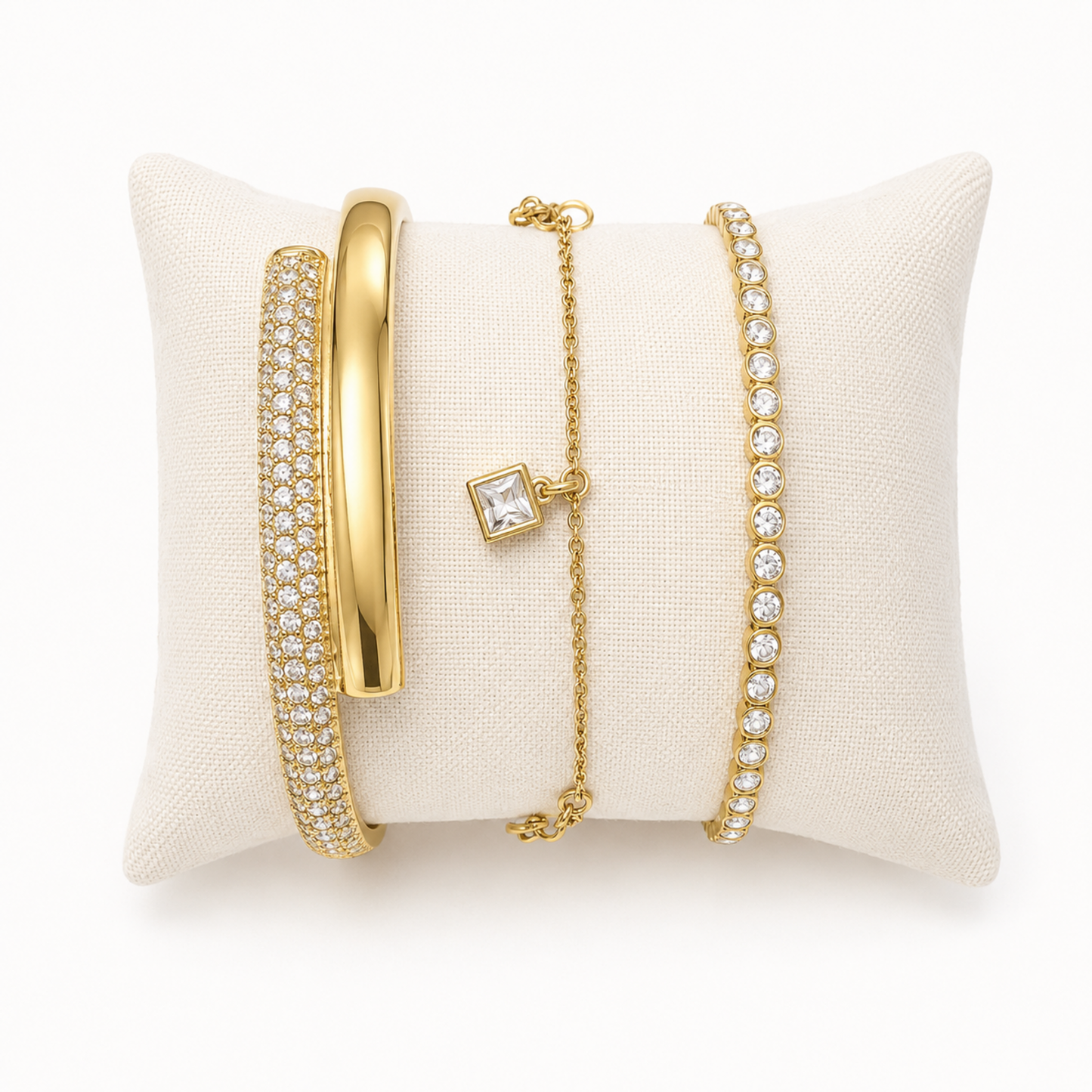 A premium three-piece gold-plated bracelet stack for women featuring a thick half-pavé crossover bangle, a sleek bezel-set crystal bangle, and a fine chain bracelet with three dangling square crystal charms.