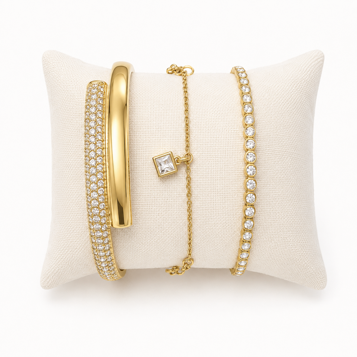A premium three-piece gold-plated bracelet stack for women featuring a thick half-pavé crossover bangle, a sleek bezel-set crystal bangle, and a fine chain bracelet with three dangling square crystal charms.