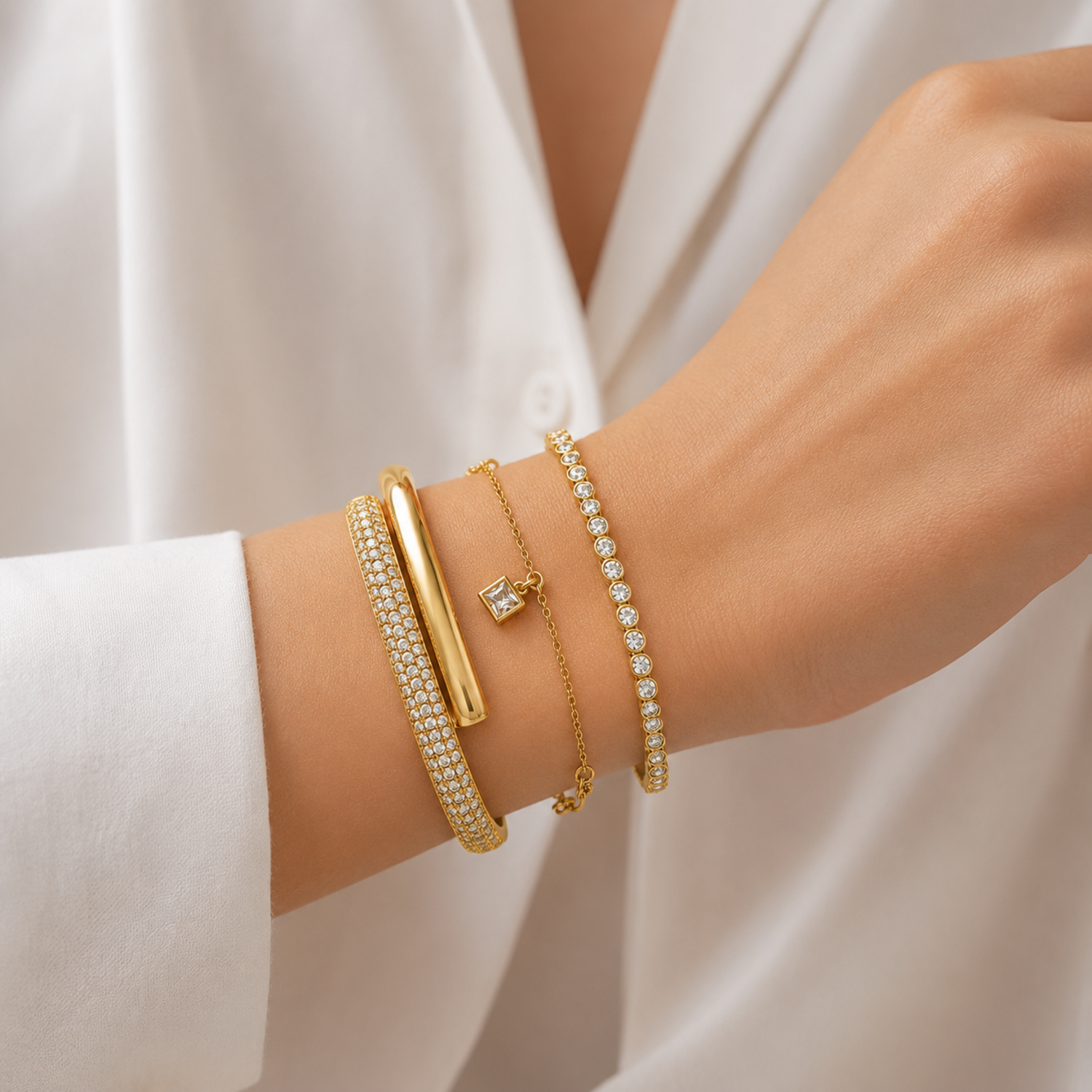 A premium three-piece gold-plated bracelet stack for women featuring a thick half-pavé crossover bangle, a sleek bezel-set crystal bangle, and a fine chain bracelet with three dangling square crystal charms on a model