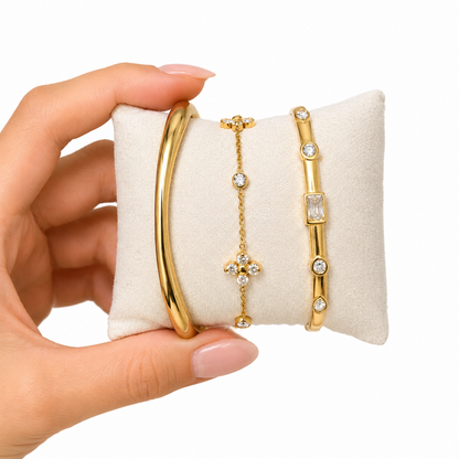 A close-view of a premium three-piece gold-plated bracelet stack for women featuring a thick polished dome bangle, a delicate crystal flower charm chain, and a sleek baguette station bangle