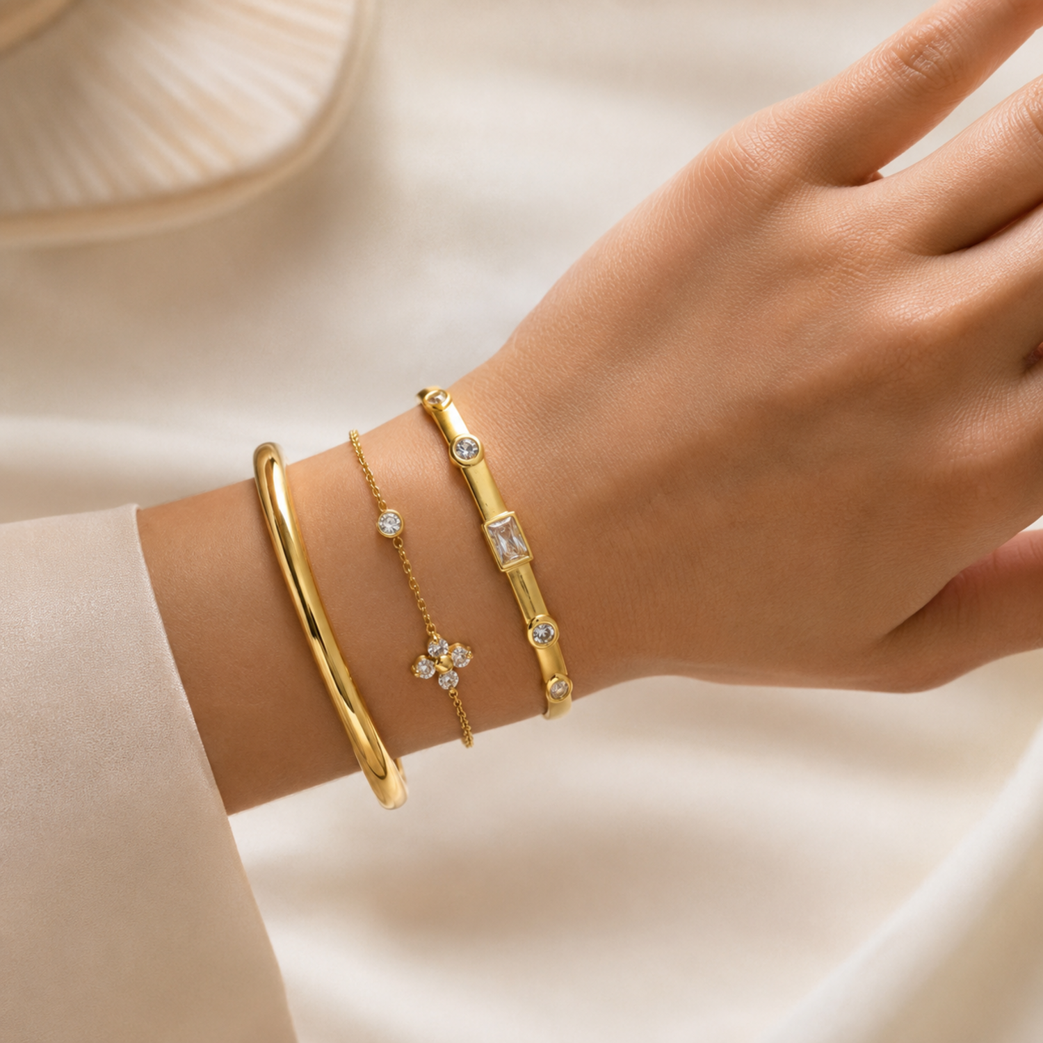 A premium three-piece gold-plated bracelet stack for women featuring a thick polished dome bangle, a delicate crystal flower charm chain, and a sleek baguette station bangle, on a model