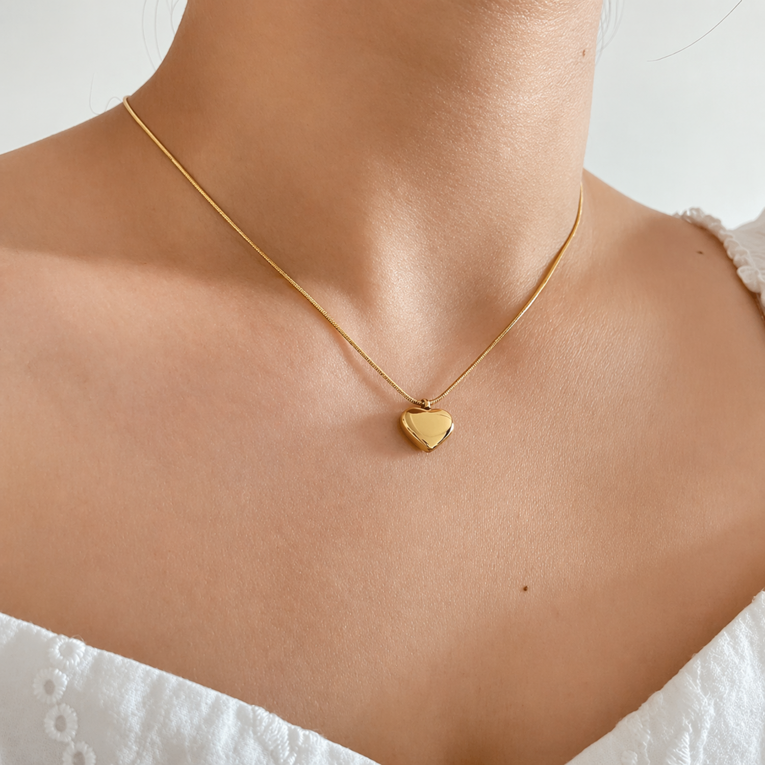 A gold-plated stainless steel chain for women featuring a small, polished 3D puffed heart pendant on a delicate link chain shown on a model