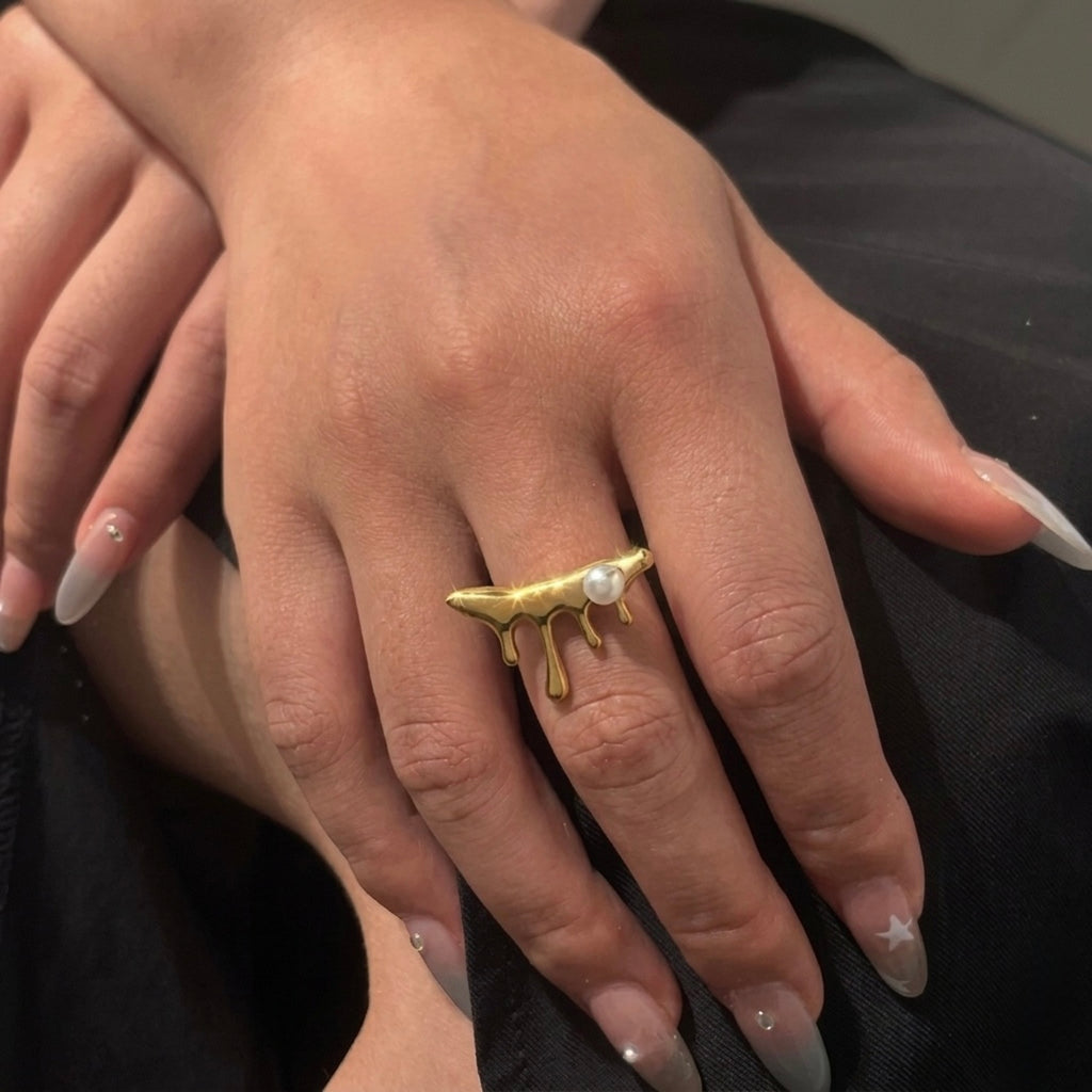 A unique 18kt gold plated stainless steel adjustable ring for women featuring a molten gold drip design with a single white pearl displayed on a model hand