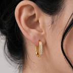 A gold-plated rectangular hoop earrings for women featuring a vertical row of clear crystals, shown on a model
