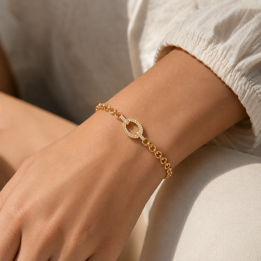A gold-plated chain bracelet for women featuring a large central oval link encrusted with crystals and round polished chain links, shown on a model