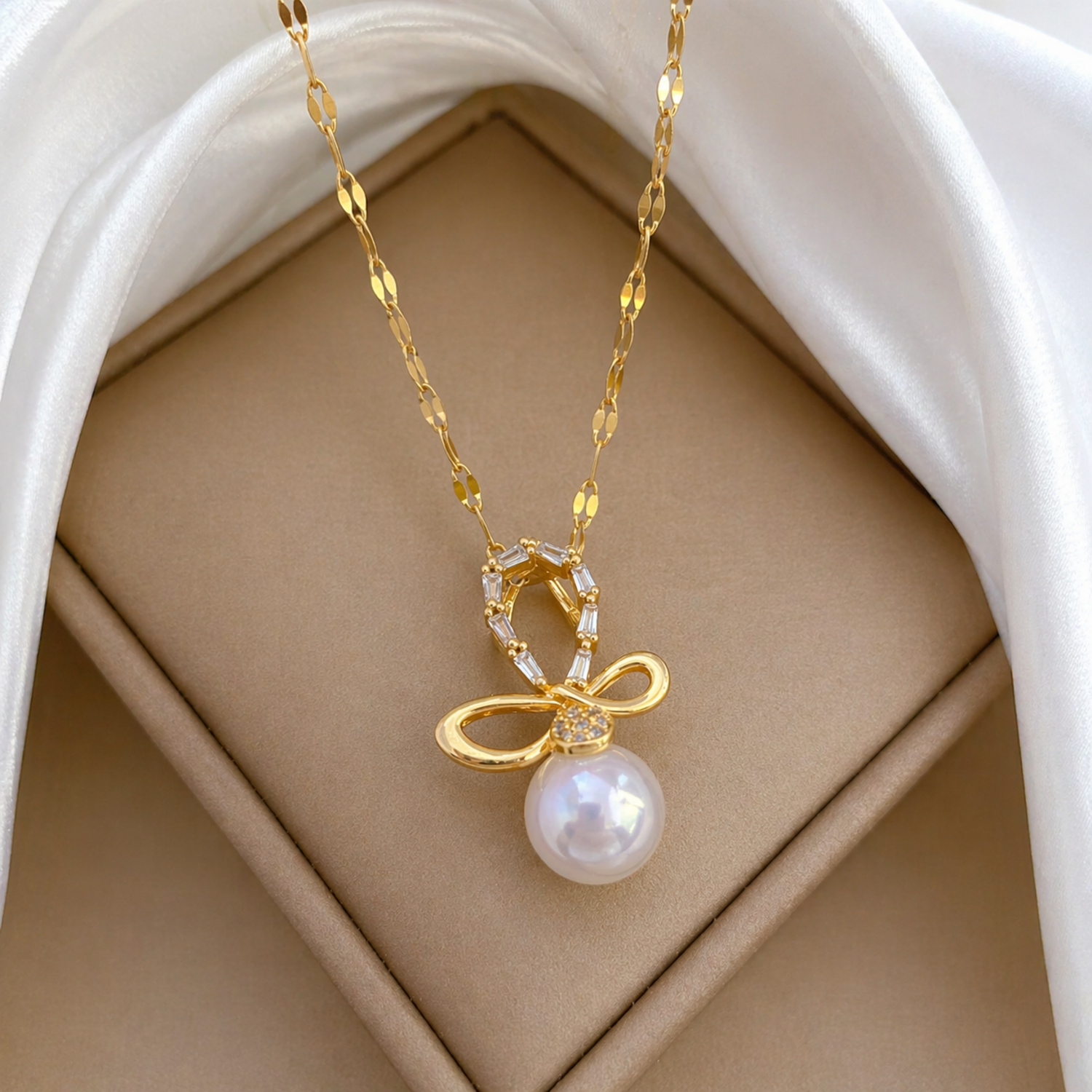 A close-view of a gold-plated stainless steel chain for women featuring a crystal-encrusted bow pendant with a large white pearl drop