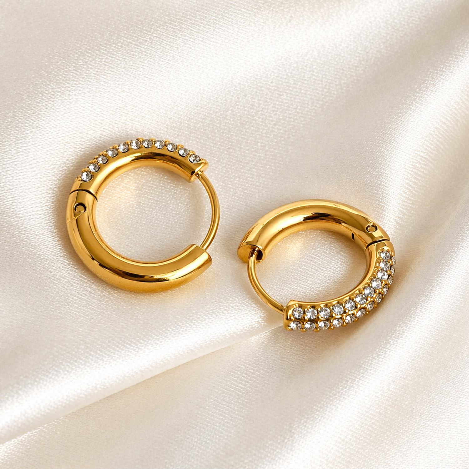 A close-view of a pair of gold-plated thick hoop earrings for women featuring a front half encrusted with clear pavé crystals