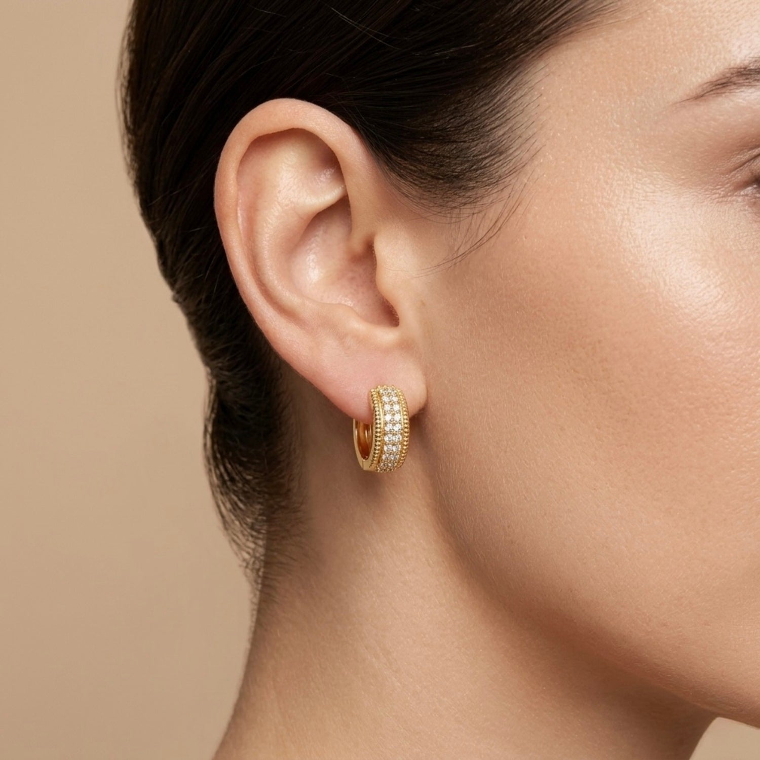 A gold-plated textured hoop earrings for women featuring a central row of clear crystals and ridged outer bands, on a model