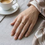 A dainty 18kt gold plated stainless steel adjustable ring for women featuring three small clear white stones and a gold bead on a model hand