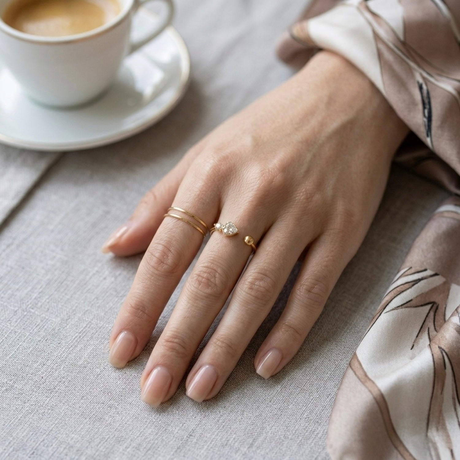 A dainty 18kt gold plated stainless steel adjustable ring for women featuring three small clear white stones and a gold bead on a model hand