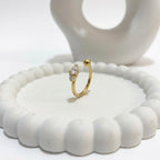 A dainty 18kt gold plated stainless steel adjustable ring for women featuring three small clear white stones and a gold bead on a white aesthetic jewelry tray