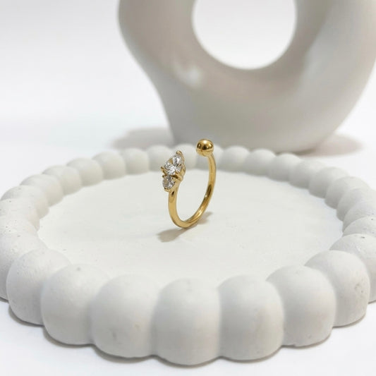 A dainty 18kt gold plated stainless steel adjustable ring for women featuring three small clear white stones and a gold bead on a white aesthetic jewelry tray