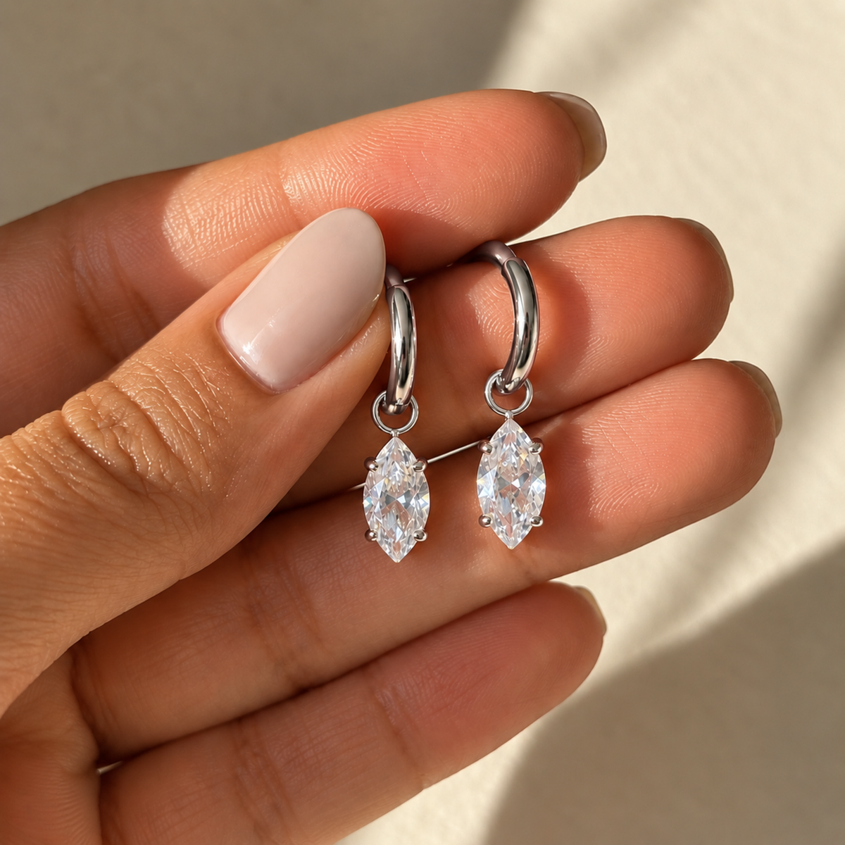 A close-view of a drop hoop earrings with marquise-cut clear crystals, available in silver