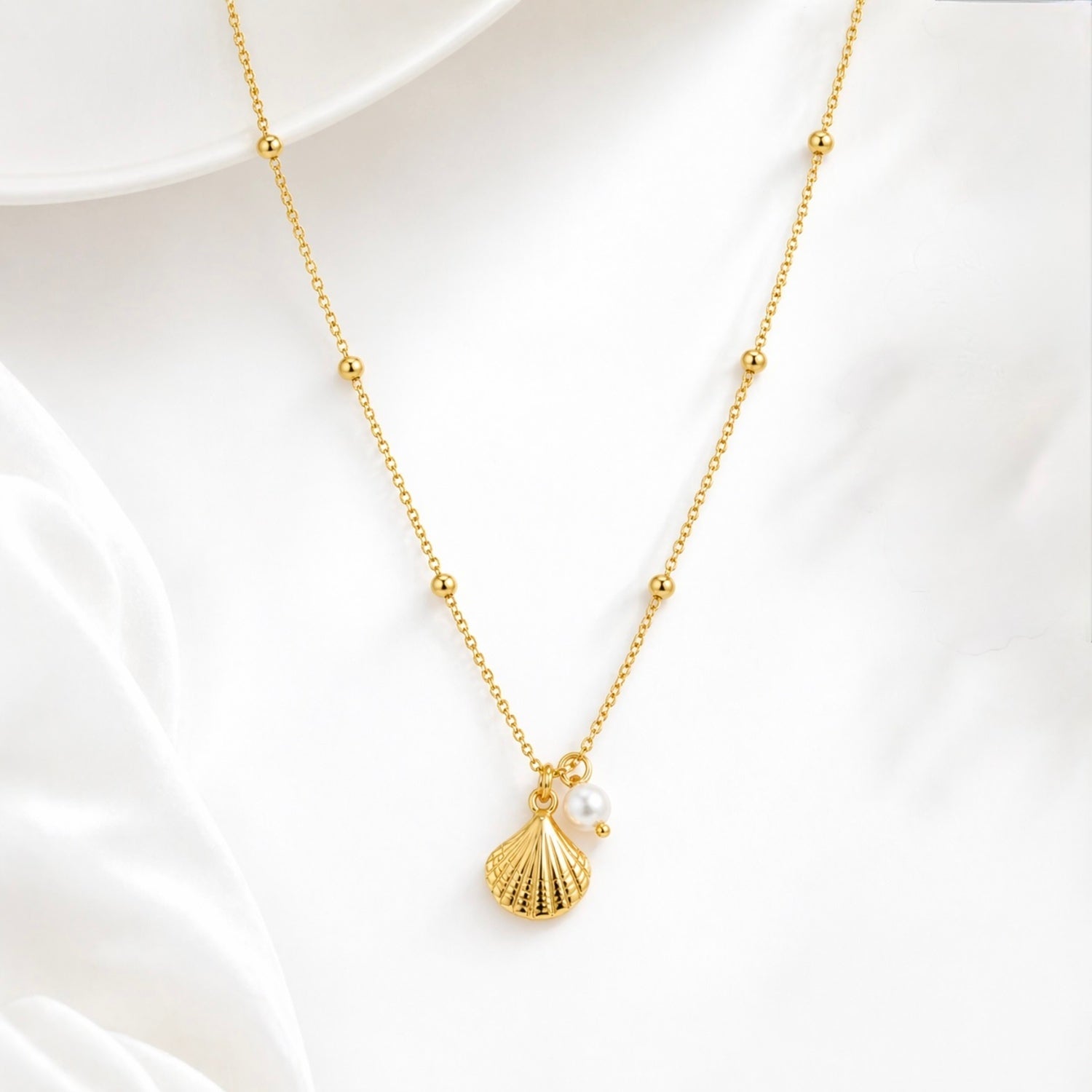 A gold-plated stainless steel chain for women featuring small bead stations and a shell pendant with a single pearl, set against a white background