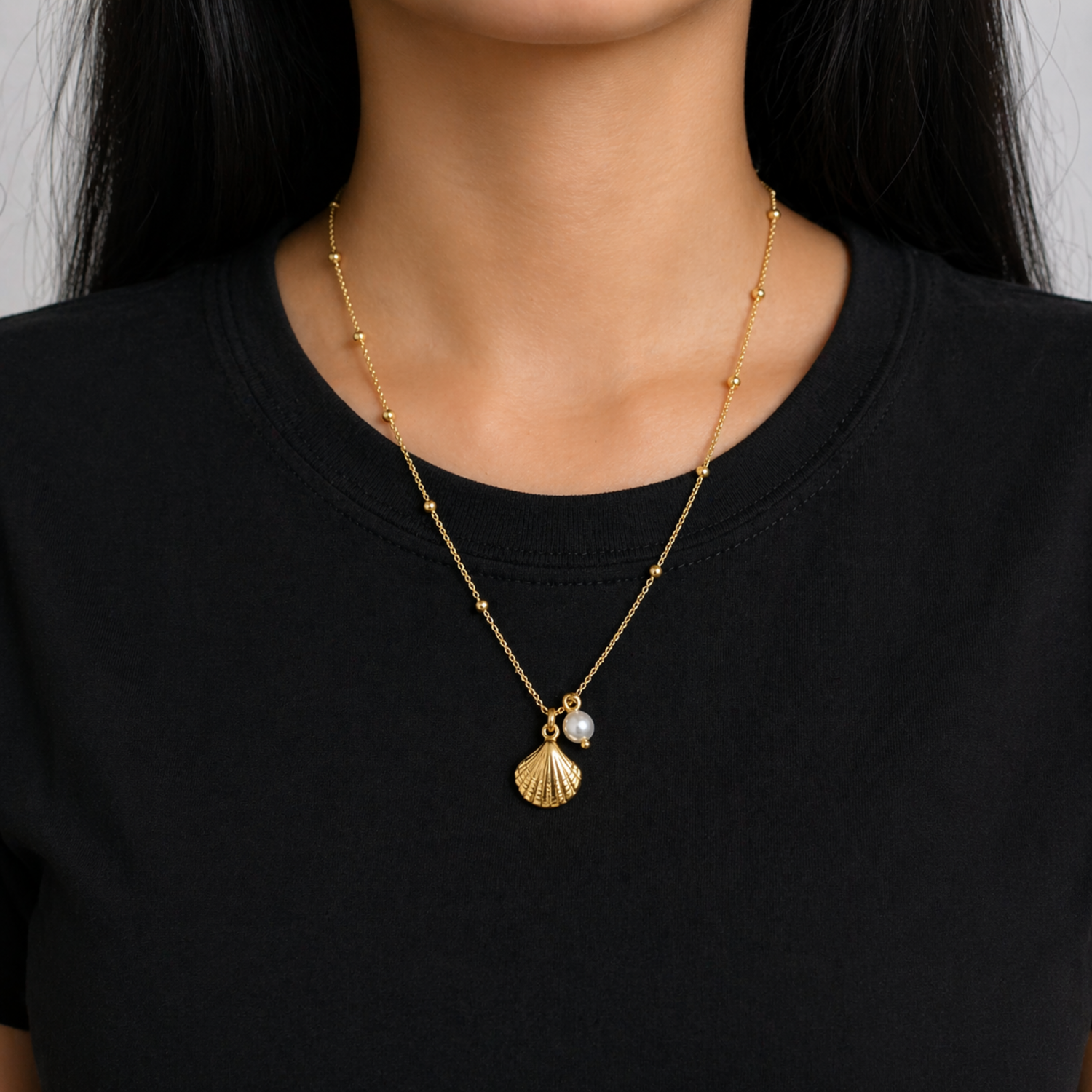 A gold-plated stainless steel chain for women featuring small bead stations and a shell pendant with a single pearl, shown on a model