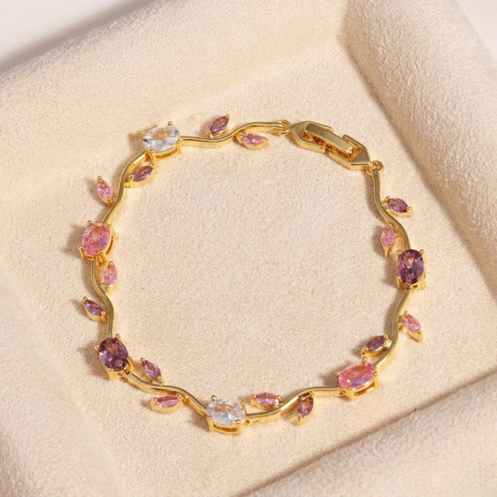 A close-view of a gold-plated floral vine chain bracelet for women featuring lavender, pink, and clear oval and marquise-cut stones, shown on a beige background