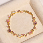 A close-view of a gold-plated floral vine chain bracelet for women featuring lavender, pink, and clear oval and marquise-cut stones, shown on a beige background