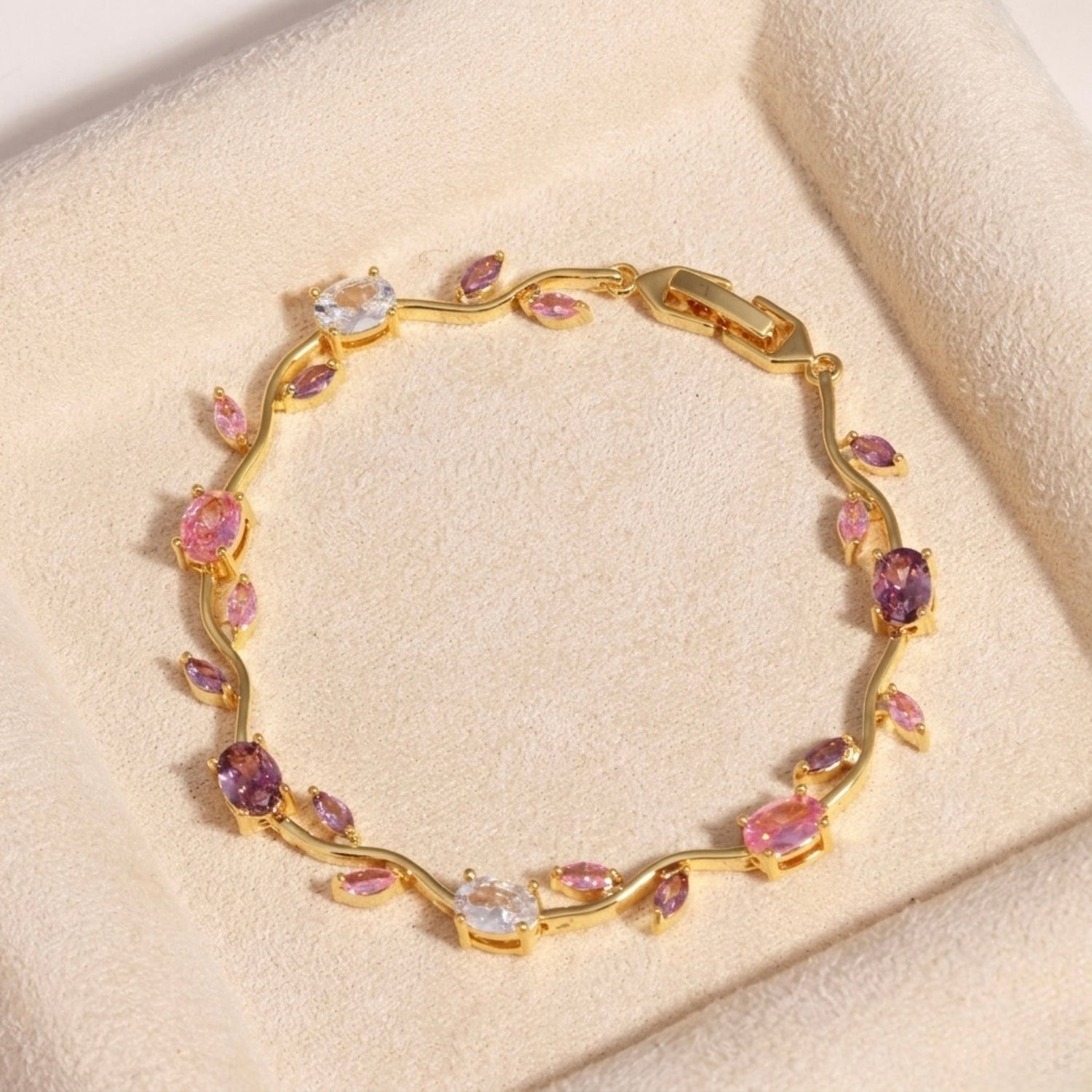 A close-view of a gold-plated floral vine chain bracelet for women featuring lavender, pink, and clear oval and marquise-cut stones, shown on a beige background