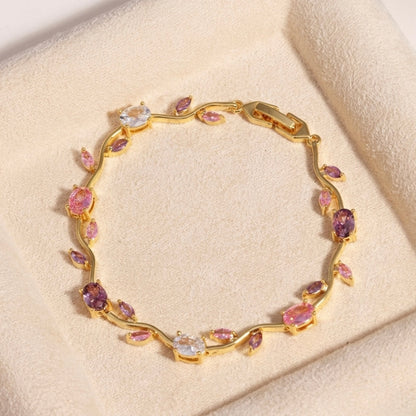 A close-view of a gold-plated floral vine chain bracelet for women featuring lavender, pink, and clear oval and marquise-cut stones, shown on a beige background