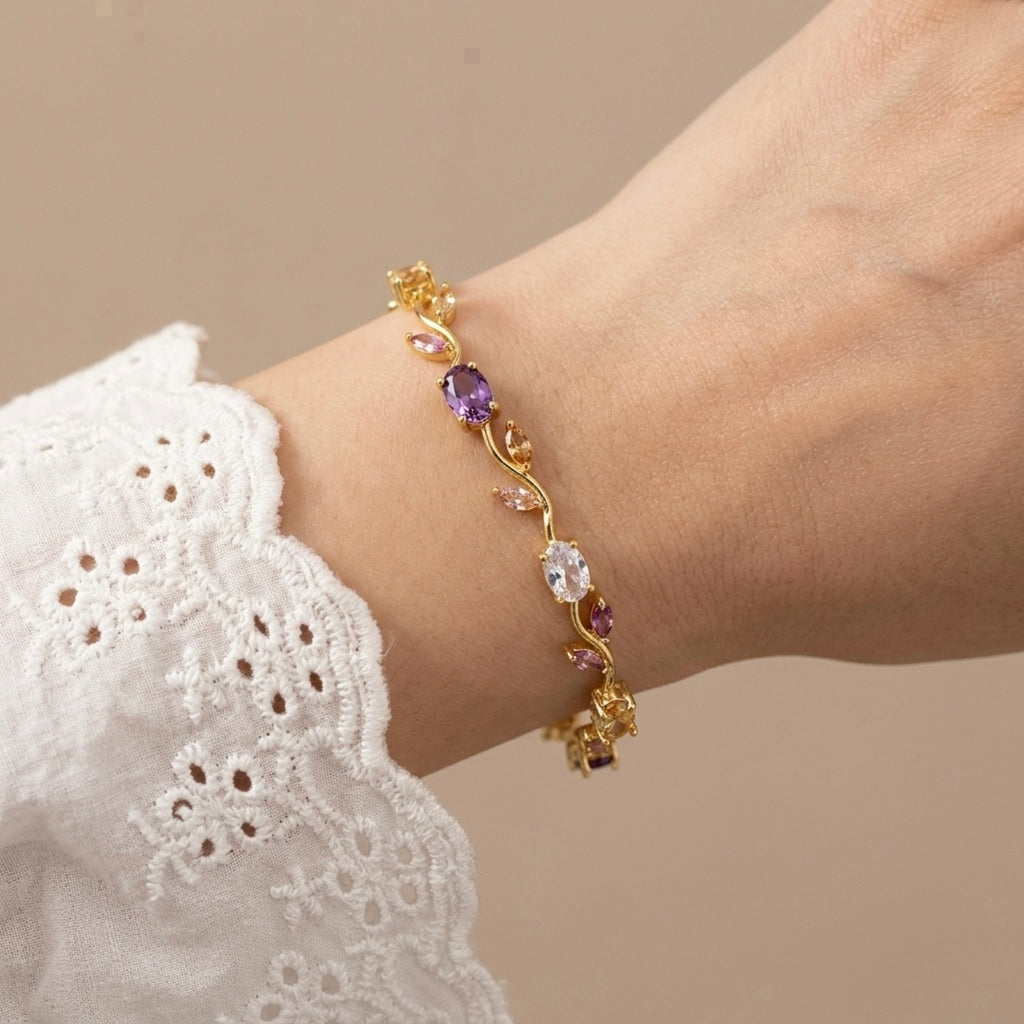 A gold-plated floral vine chain bracelet for women featuring lavender, pink, and clear oval and marquise-cut stones, shown on a model