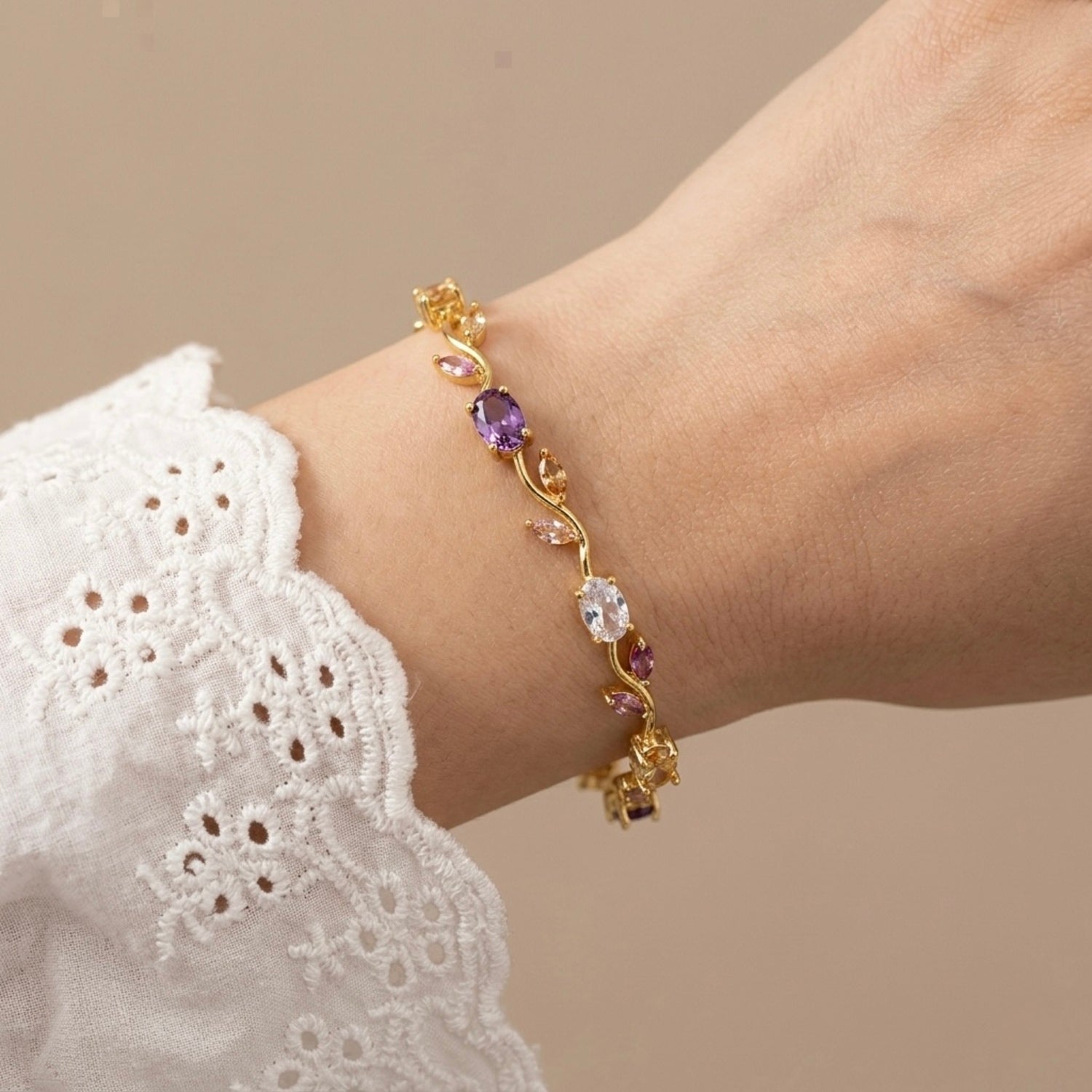A gold-plated floral vine chain bracelet for women featuring lavender, pink, and clear oval and marquise-cut stones, shown on a model