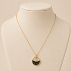 A gold-plated stainless steel chain for women featuring a circular pendant with black enamel wave patterns and a single floating crystal