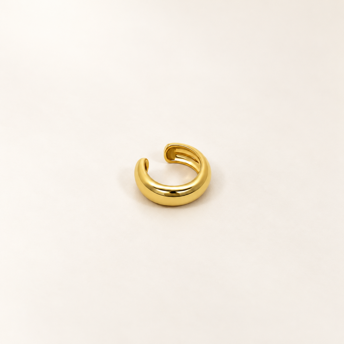 A close-view of a Gold-tone open ear cuff with a smooth rounded band and a row of clear crystals along the lower edge.