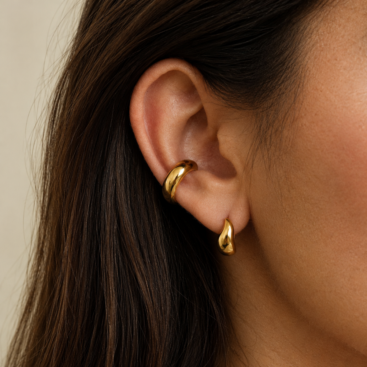 Gold-tone open ear cuff with a smooth rounded band and a row of clear crystals along the lower edge, on a model