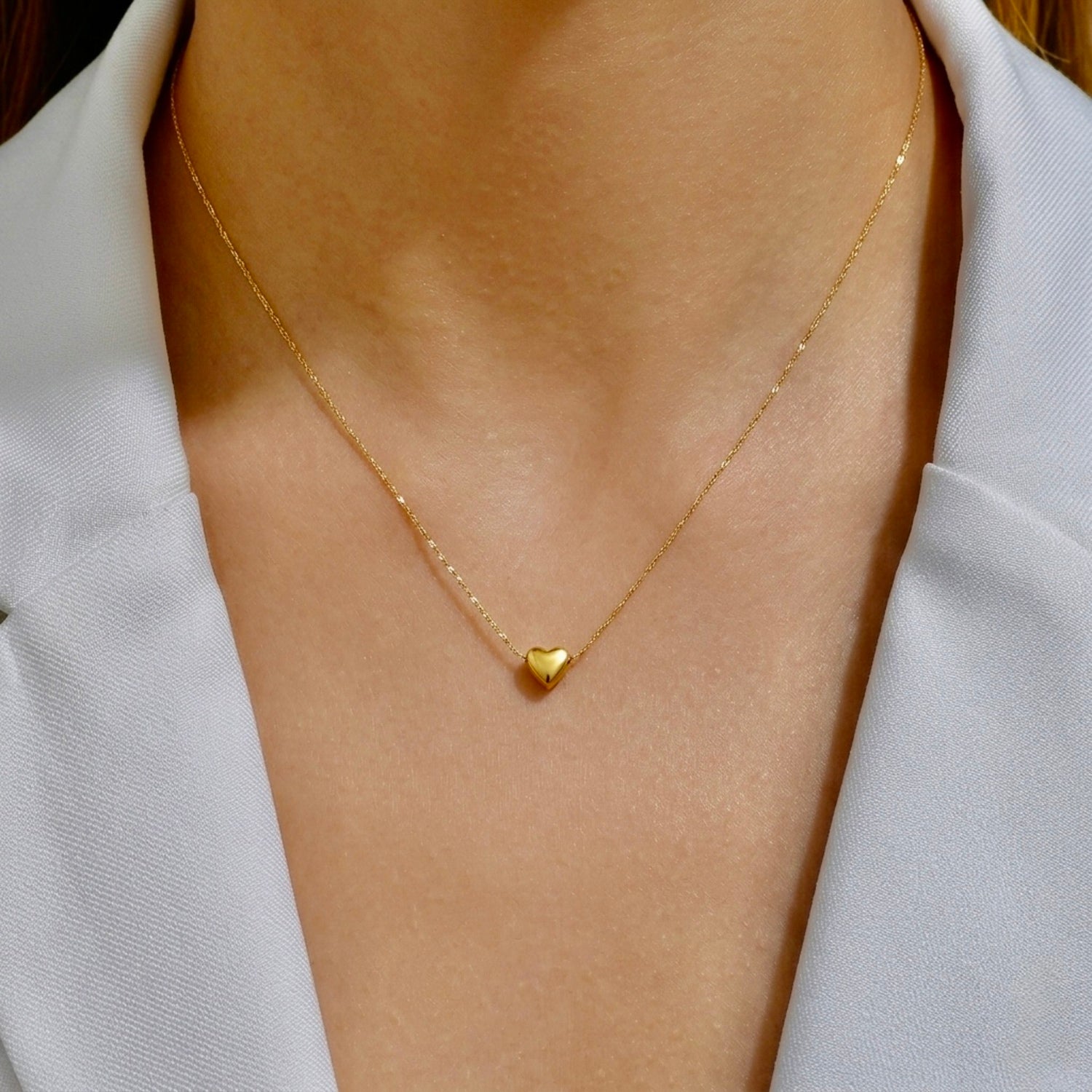A gold-plated stainless steel chain for women featuring a tiny, puffed heart pendant on a delicate link chain shown on a model