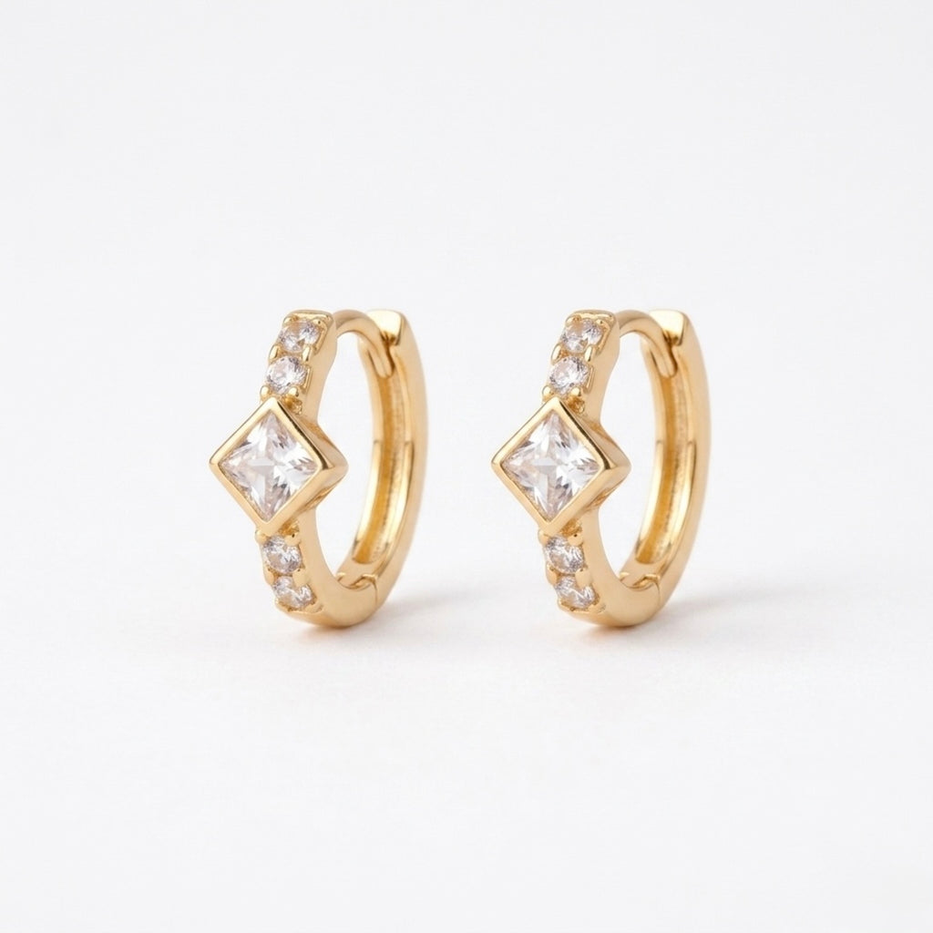 A pair of gold-plated huggie hoop earrings for women featuring a central kite-set princess-cut clear crystal, shown on a clean white background.