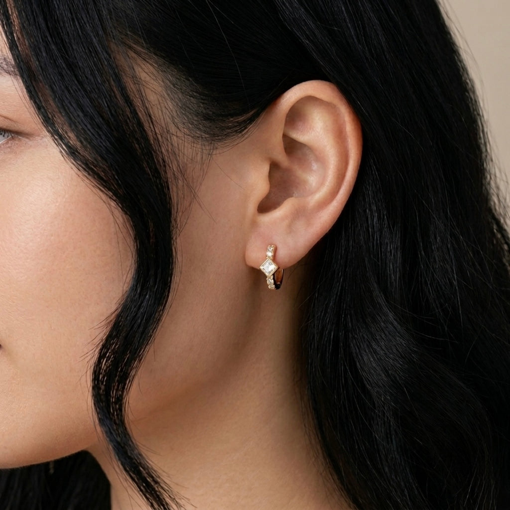 A gold-plated huggie hoop earrings for women featuring a central kite-set princess-cut clear crystal, shown on a model