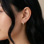 A gold-plated huggie hoop earrings for women featuring a central kite-set princess-cut clear crystal, shown on a model