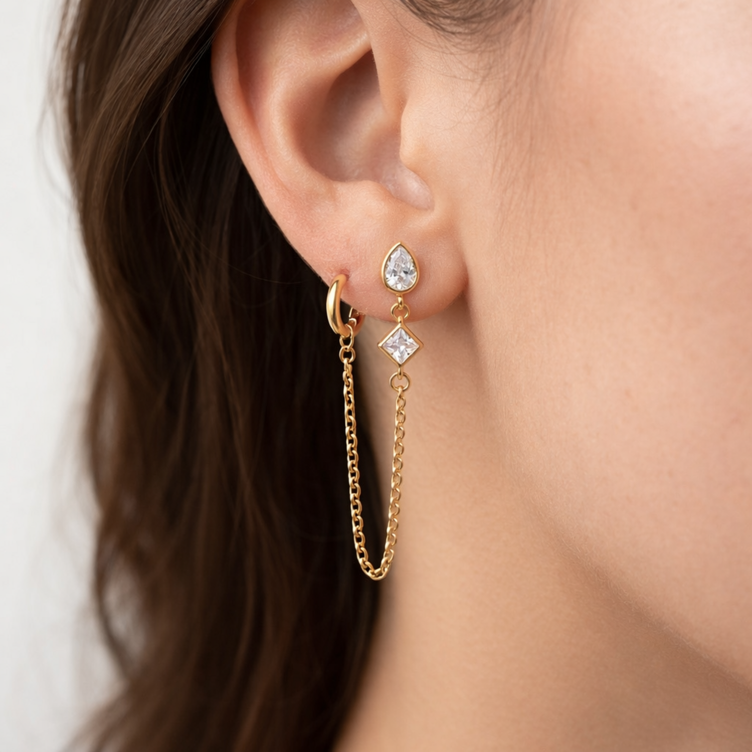 A gold-plated ear chain earrings for women connecting a tiered crystal drop stud to a small gold hoop with a fine chain  shown on a model