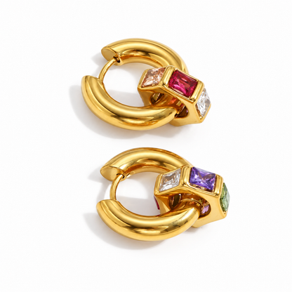 A pair of gold huggie hoop earrings with a square bezel-set multicolor gemstone cluster, featuring pink, purple, green, and clear stones, on a white background.