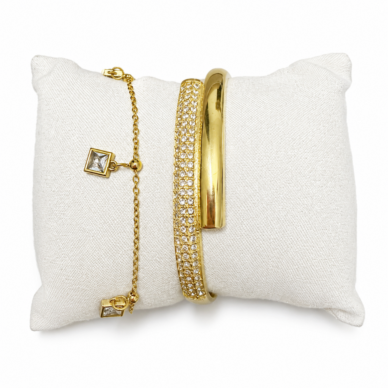 A premium two-piece gold-plated bracelet stack for women featuring a thick half-pavé crossover bangle and a fine chain bracelet with three dangling square crystal charms.